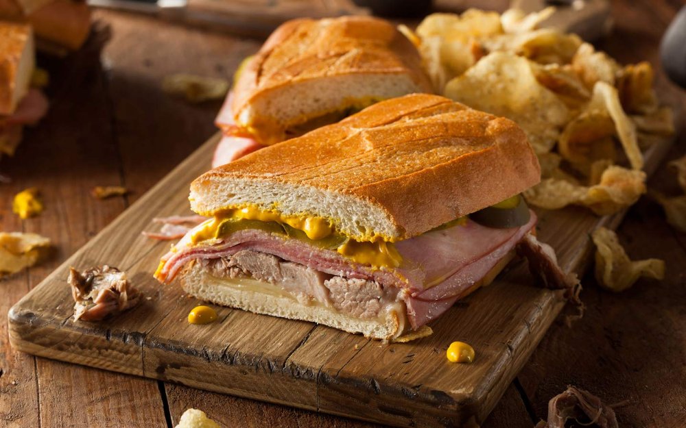 View of Cuban sandwich cut in half with a side of chips