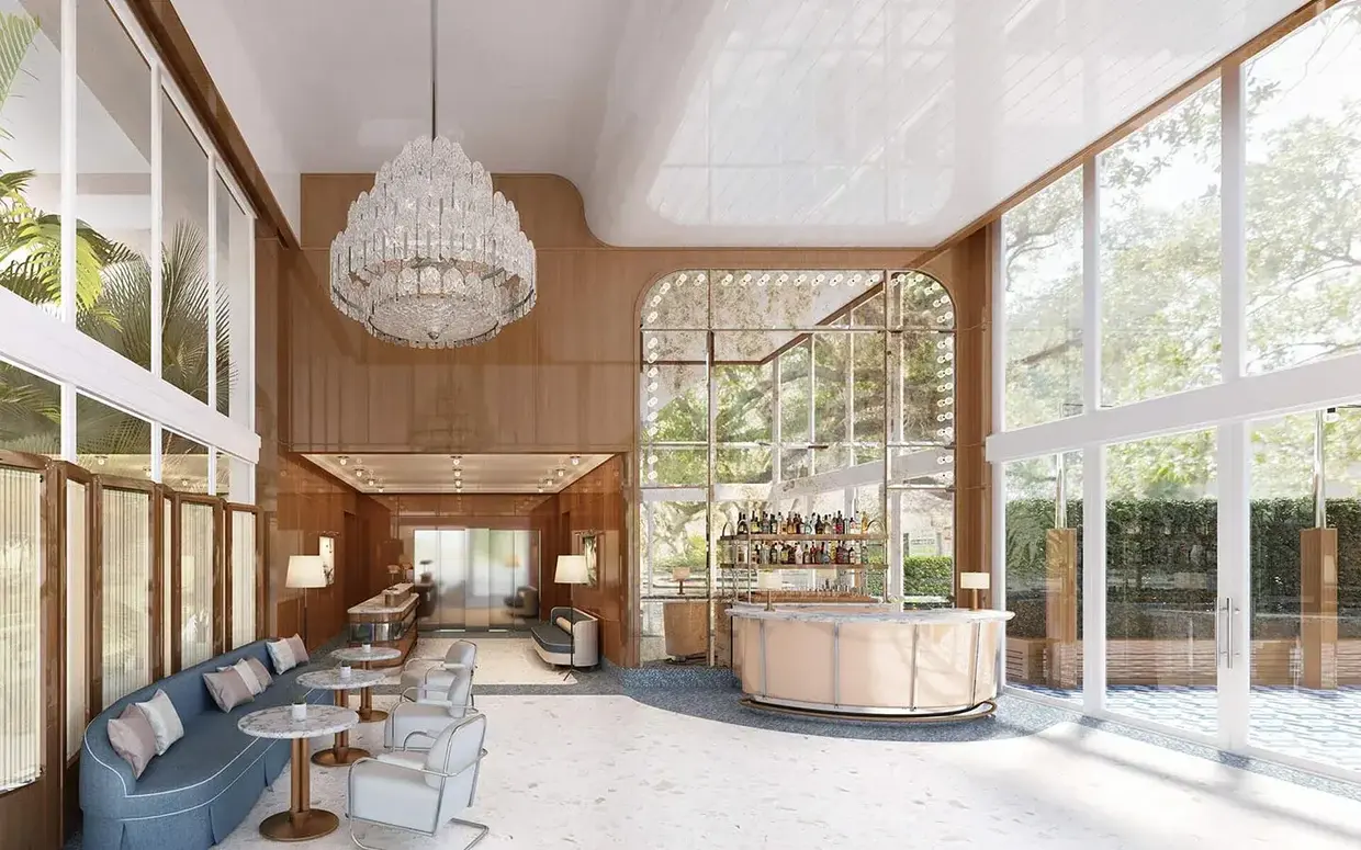 A spacious lobby with a high ceiling, a large chandelier, a bar, and a seating area, featuring large windows that let in natural light.