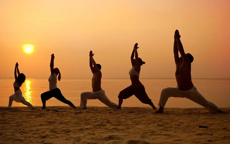 Row of people doing yoga by the ocean during sunset