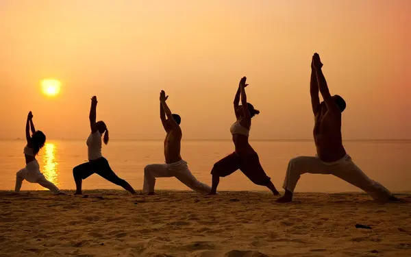 Row of people doing yoga by the ocean during sunset