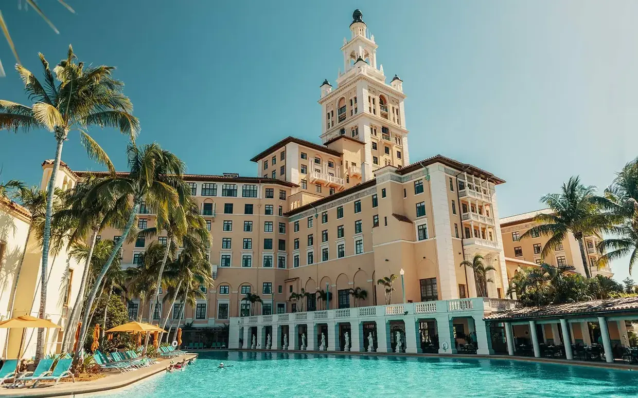 A large hotel building with a pool and palm trees in front of it.