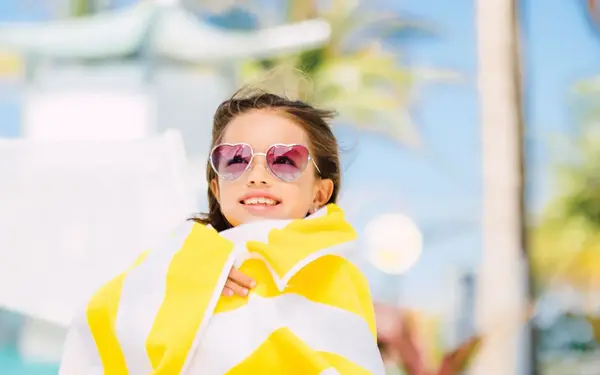 Little girl wearing sunglasses and wrapped in a beach towel