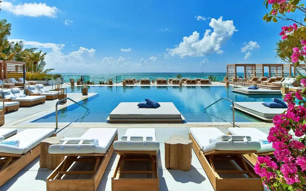A poolside area with lounge chairs, a pool, and an ocean view.