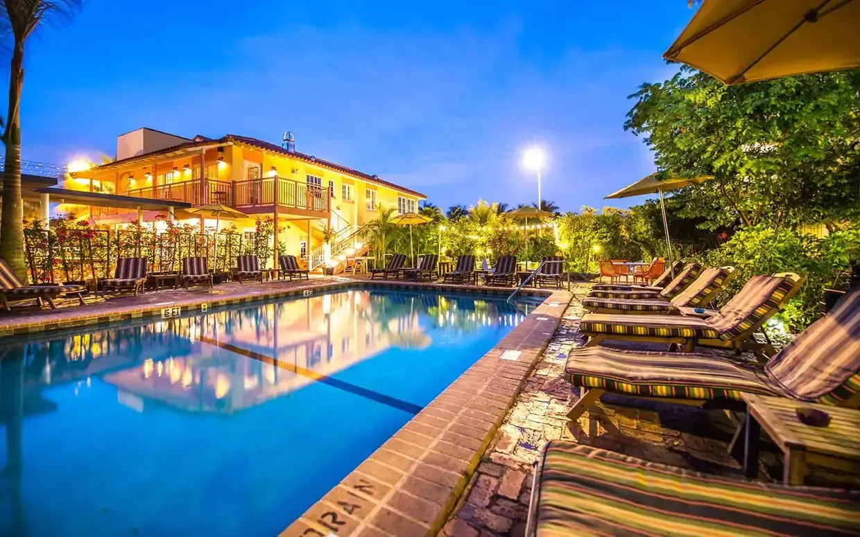 A serene poolside scene at dusk with lounge chairs, a pool, and a building in the background.