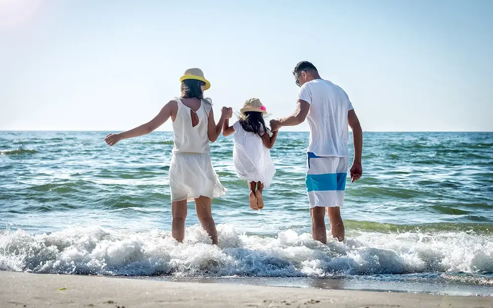 Family with child in middle swinging into ocean
