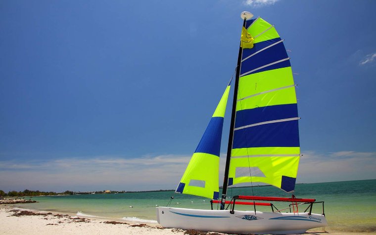 Bill Baggs Cape Florida State Park lighthouse Colorful Hobie sailboat on sandy beach with blue ocean backdrop