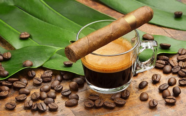 Cup of cuban coffee showcasing a cuban cigar on top of the glass with coffee beans all around Cup of cuban coffee showcasing a cuban cigar on top of the glass with coffee beans all around