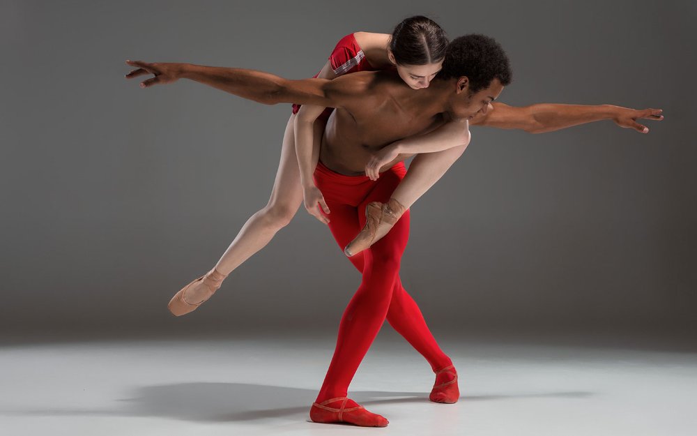 Ballet dancing couple in red, with woman on man's back