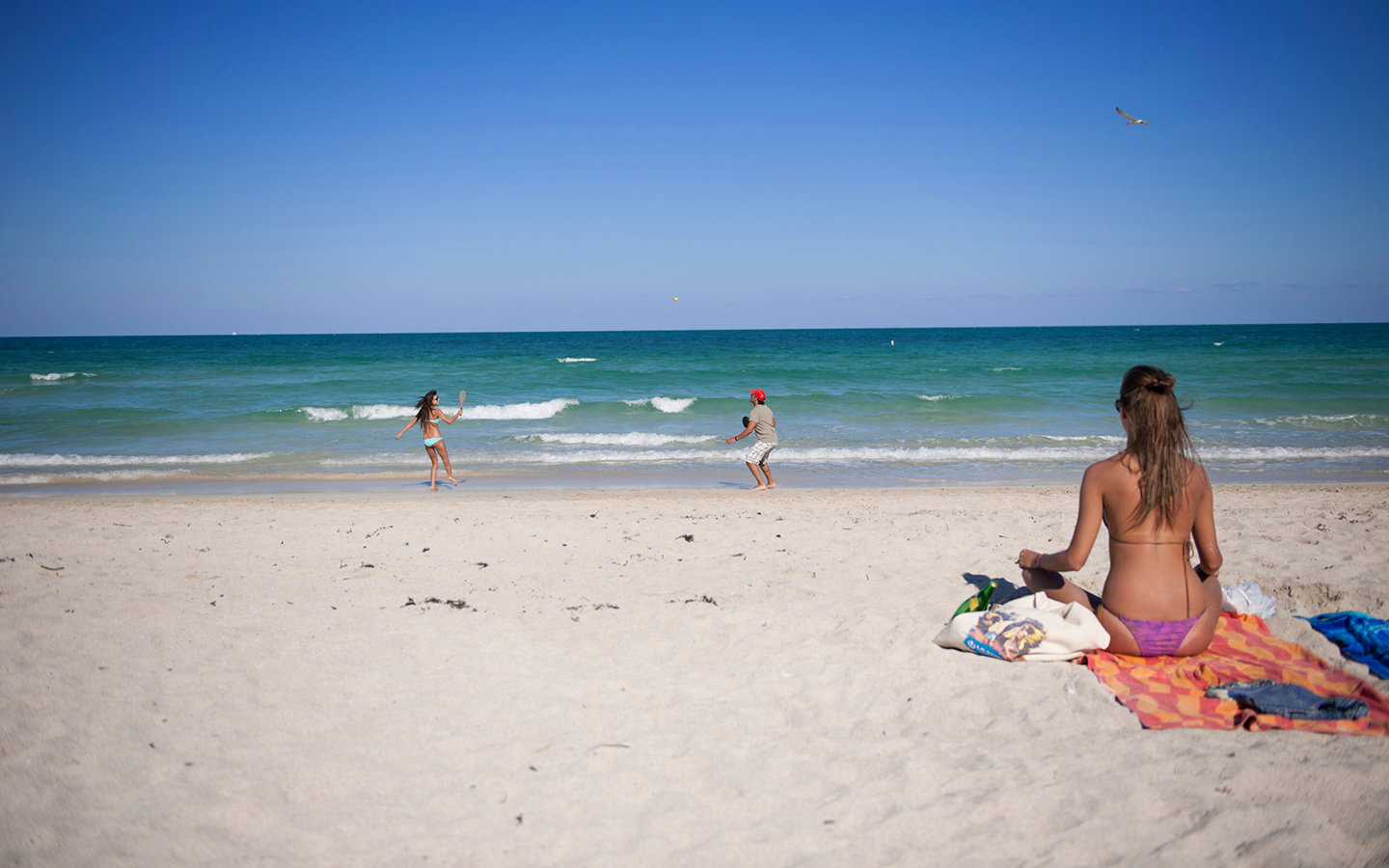 Sunbather and people playing paddleball on the beach