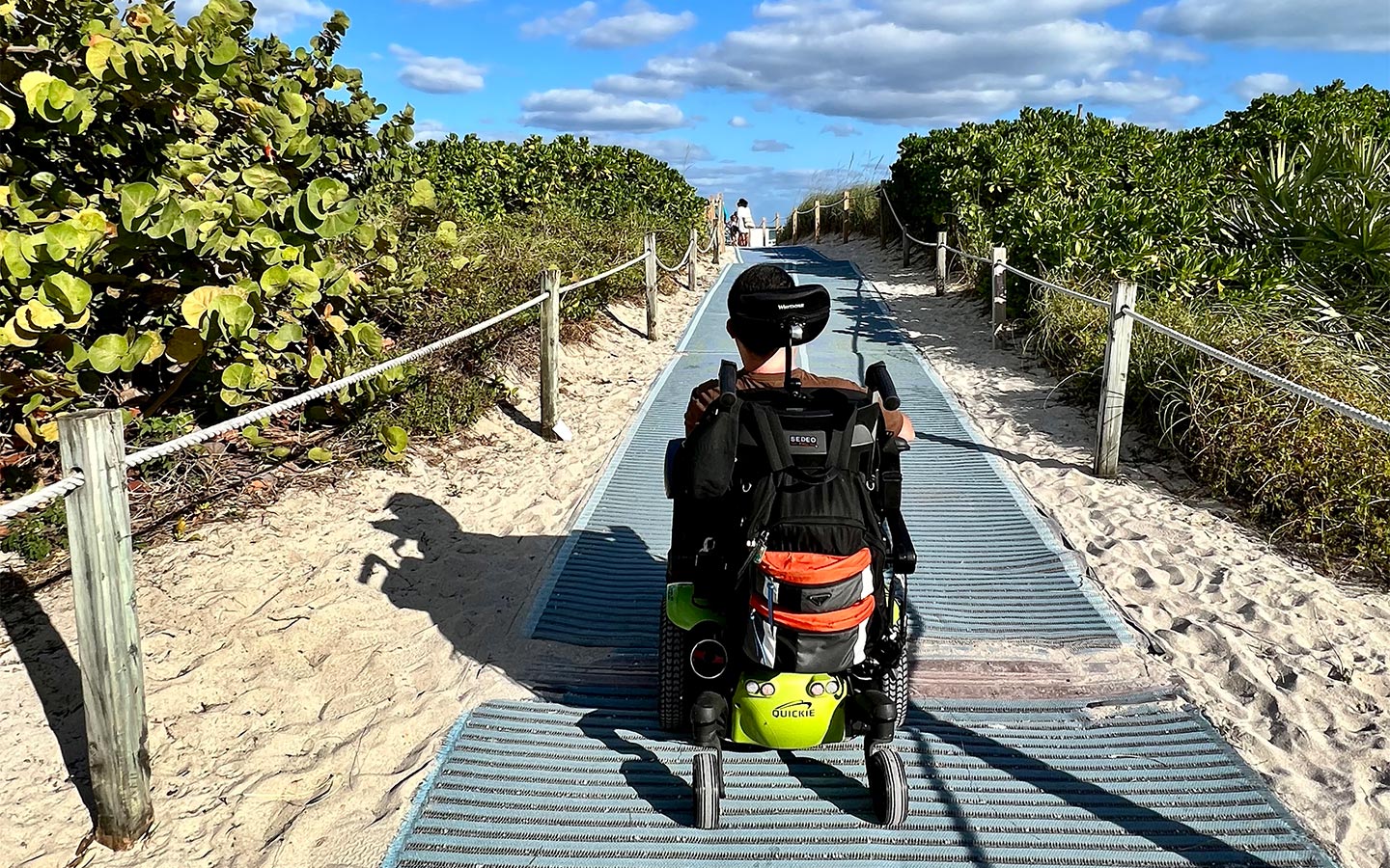 Beachgoer on wheelchair riding over smooth beach access mat.