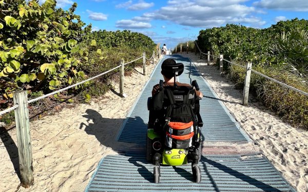 Beachgoer on wheelchair riding over smooth beach access mats.
