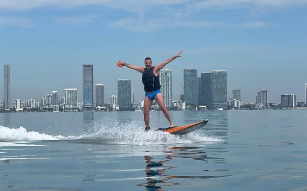 Ravi Roth surfing with a view of the Downtown Miami skyline