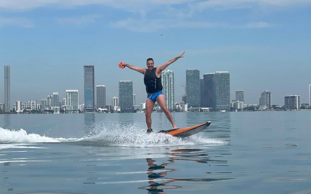 Ravi Roth surfing with a view of the Downtown Miami skyline