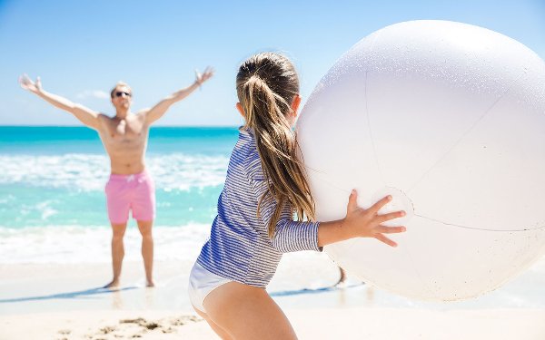 Father and daughter playing with a ball on the beach shoreline