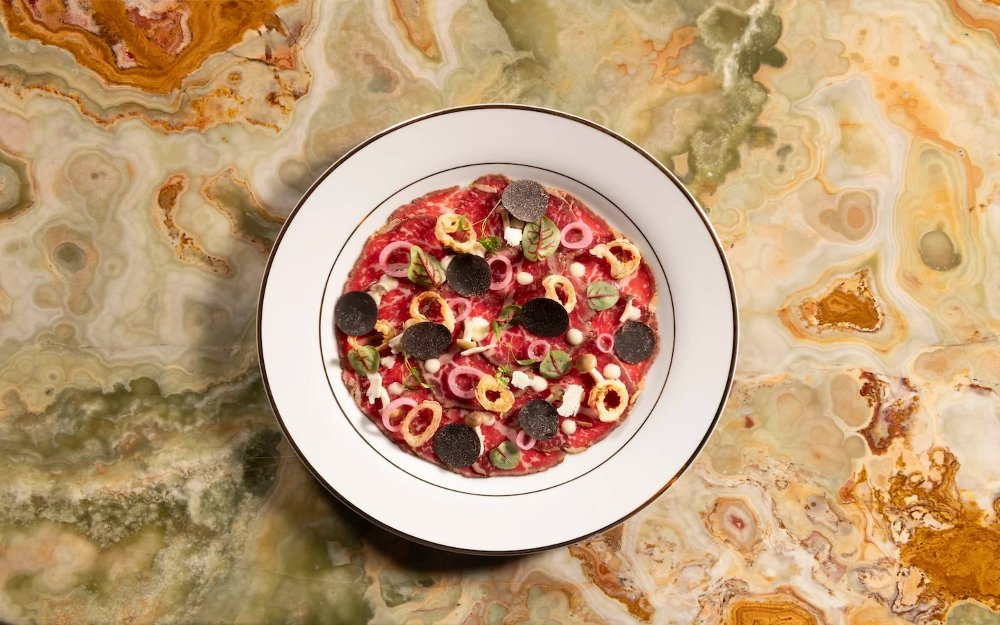 Delilah wagyu carpaccio artfully plated with fresh herbs