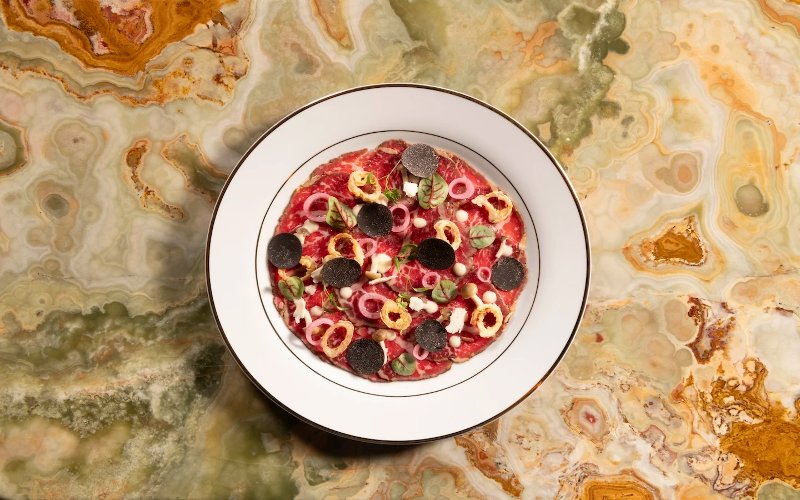 Delilah wagyu carpaccio artfully plated with fresh herbs