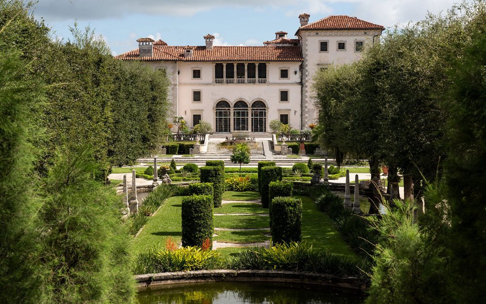 Uma visão serena de Vizcaya Museum & Gardens de dentro de seus exuberantes jardins, capturando a essência de seu charme histórico em meio à folhagem verdejante