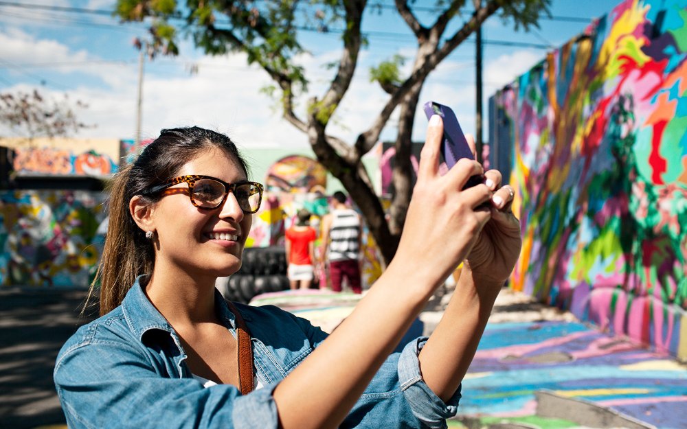 Mulher a tirar uma fotografia de um mural nas muralhas de Wynwood