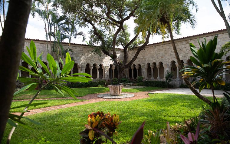 courtyard of The Ancient Spanish Monastery, featuring medieval stone arches, lush greenery, and a serene atmosphere