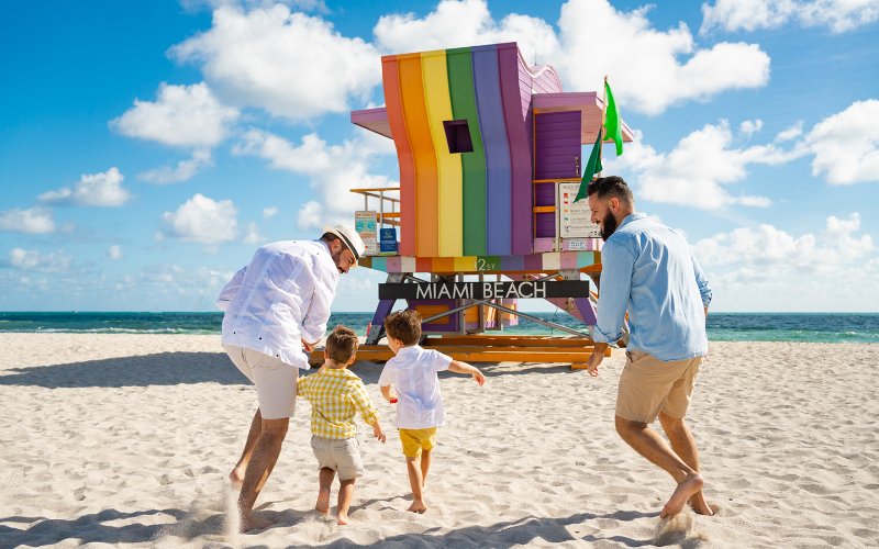 LGBTQ+ family next to a rainbow lifeguard stand on Miami Beach