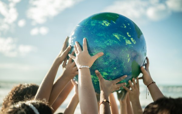 Группа детей держат большой шар, похожий на планету Земля, на Beach , ко Дню Земли
