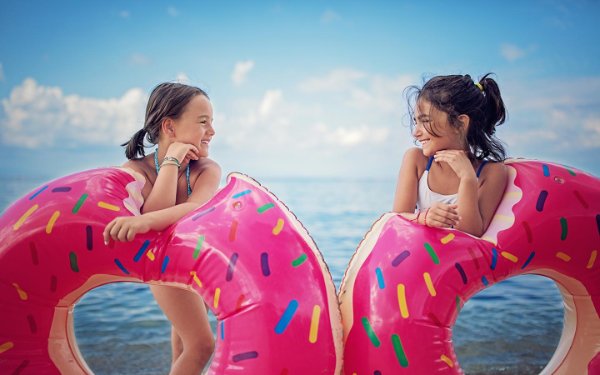 Meninas com rosquinha rosa flutuam na praia