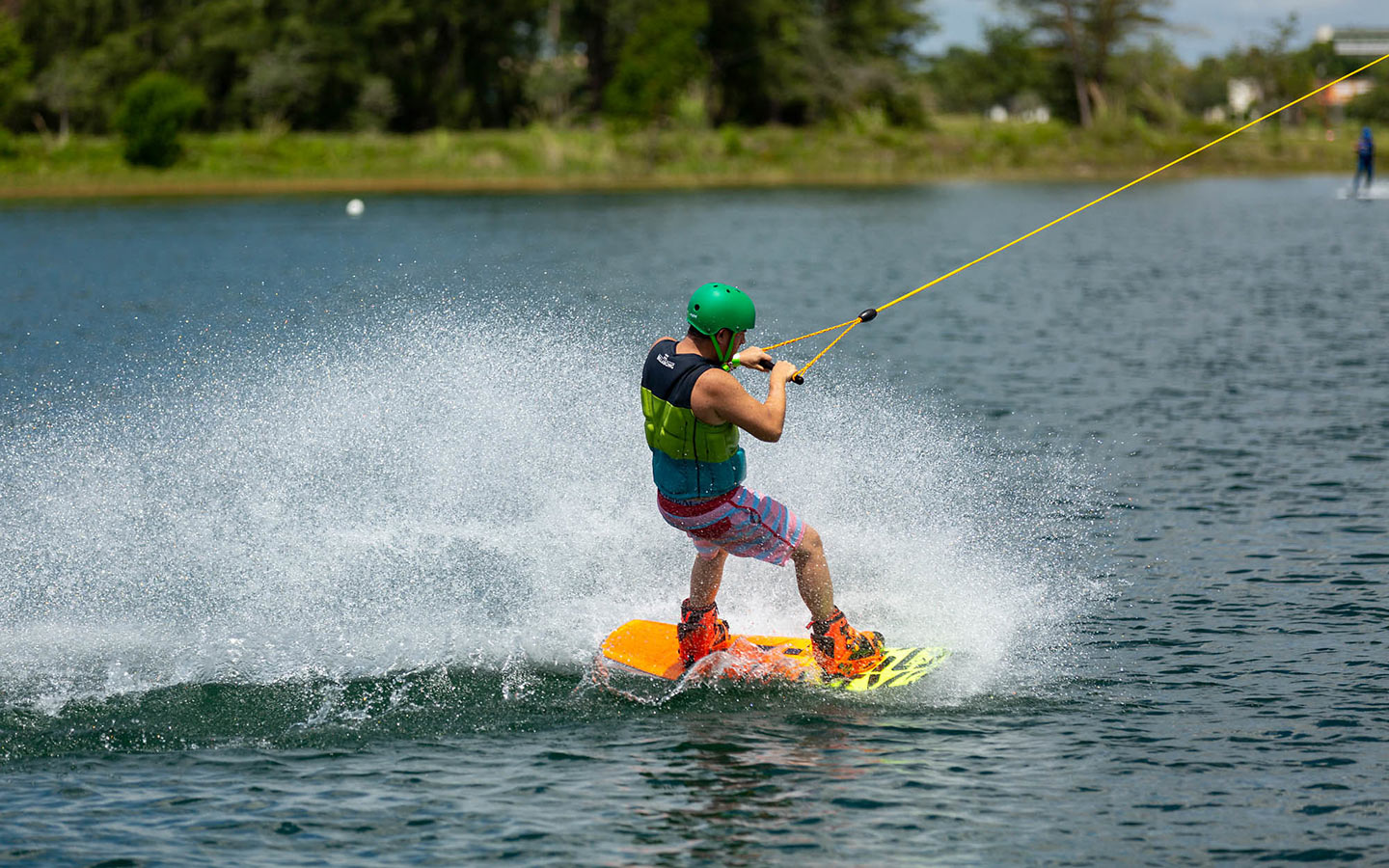 Person wakeboarding on a lake, creating a spray with lush greenery in the background Person wakeboarding on a lake, creating a spray with lush greenery in the background