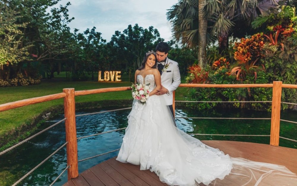 Pareja de novios junto a un estanque y un cartel de amor en Longan's Place